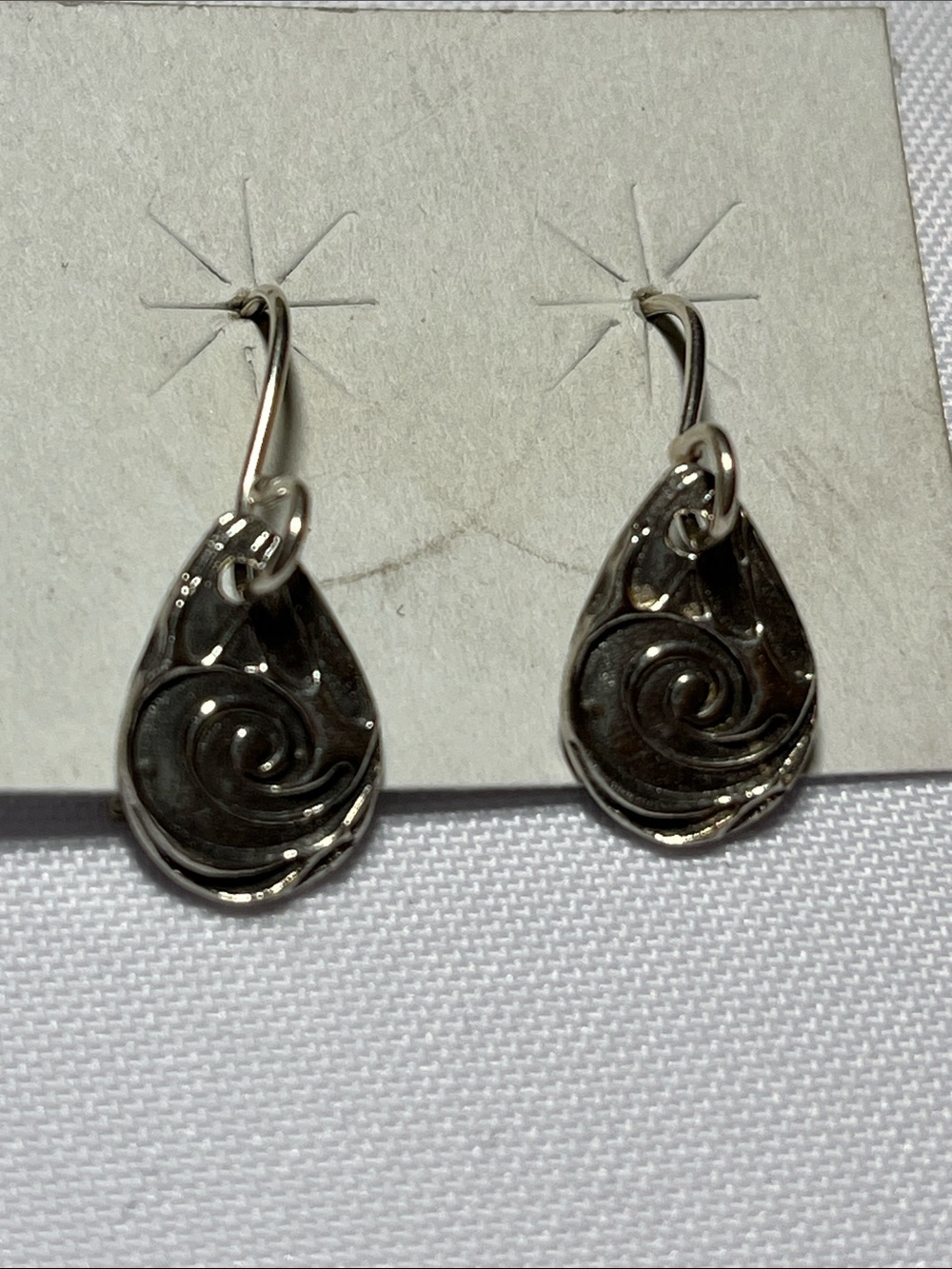 Silver dangle earring featuring a textured, teardrop-shaped charm